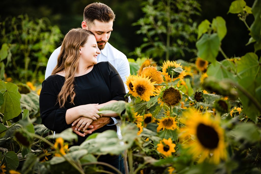 a couple cuddles in the flowers during their sunflower engagement photos