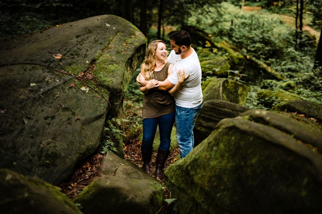 a couple hugs among large moss covered boulders during their engagement photos at Hocking Hills
