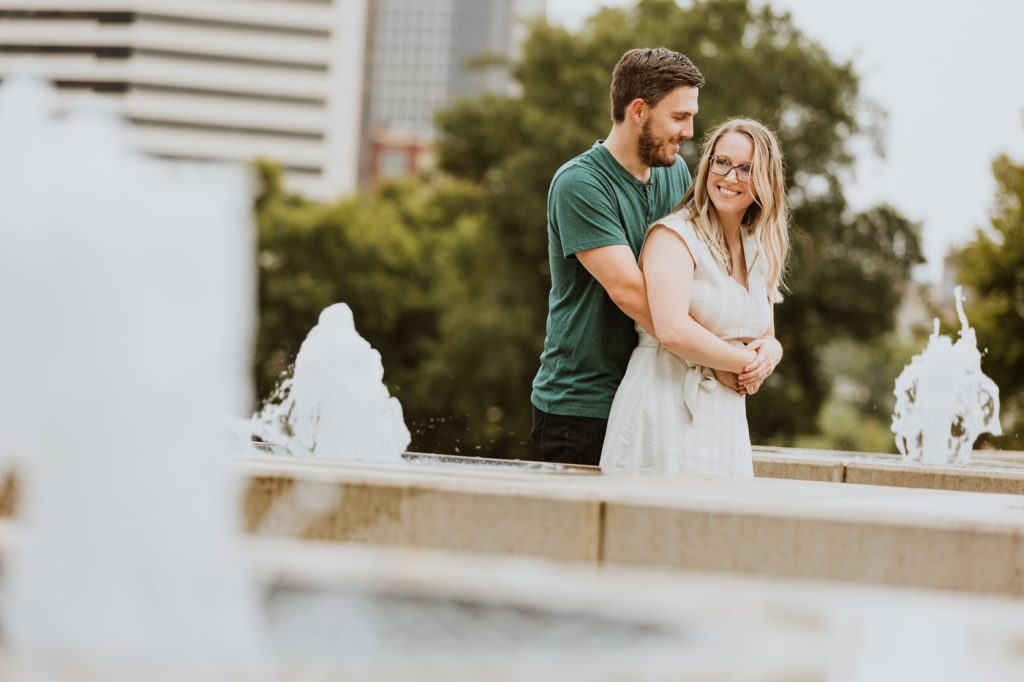 a couple snuggles by the fountains during their engagement photos at Genoa Park