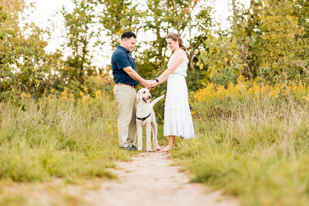 a couple plays with their dog during their engagement photos at Prairie Oaks Metro Park