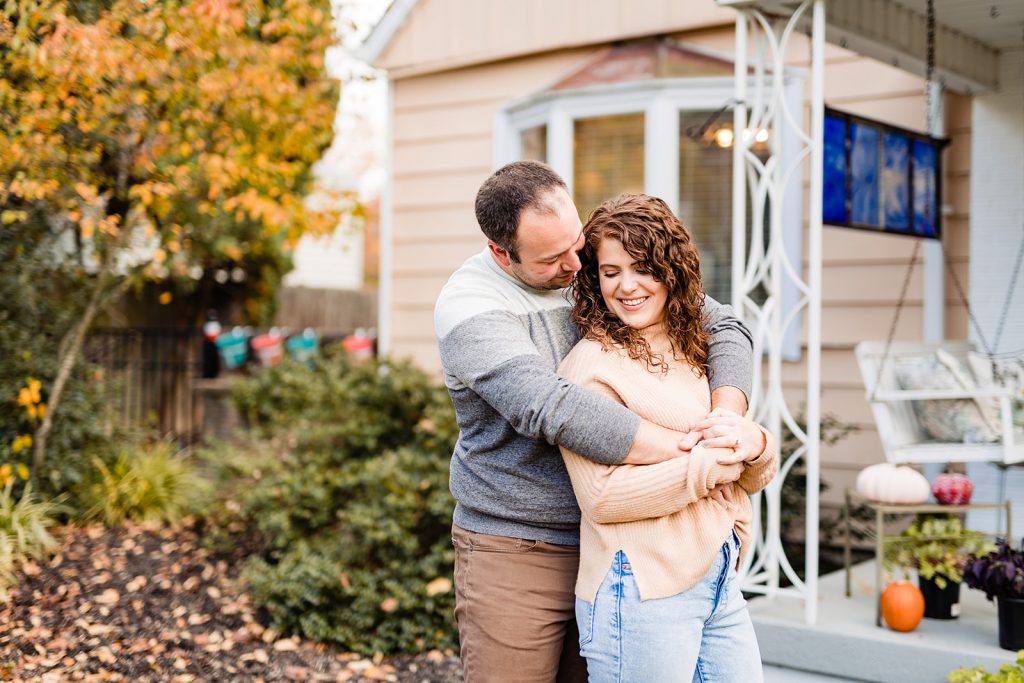 a couple cuddles in front of their house during their engagement photos in Worthington