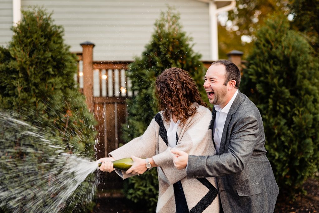 a couple sprays champagne to celebrate during their engagement photos in Worthington