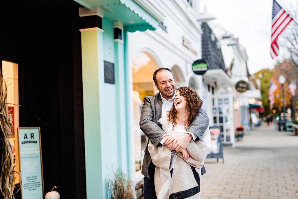 a couple cuddles in front of the colorful buildings during their engagement photos in Worthington