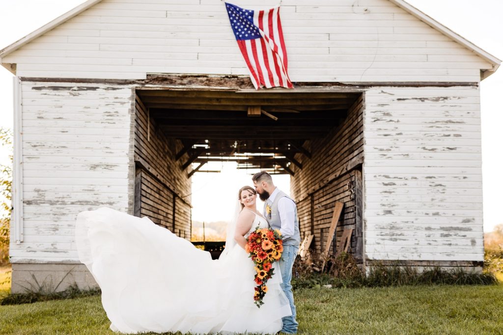 a bride and groom pose under an American flag at their Wren Farm wedding