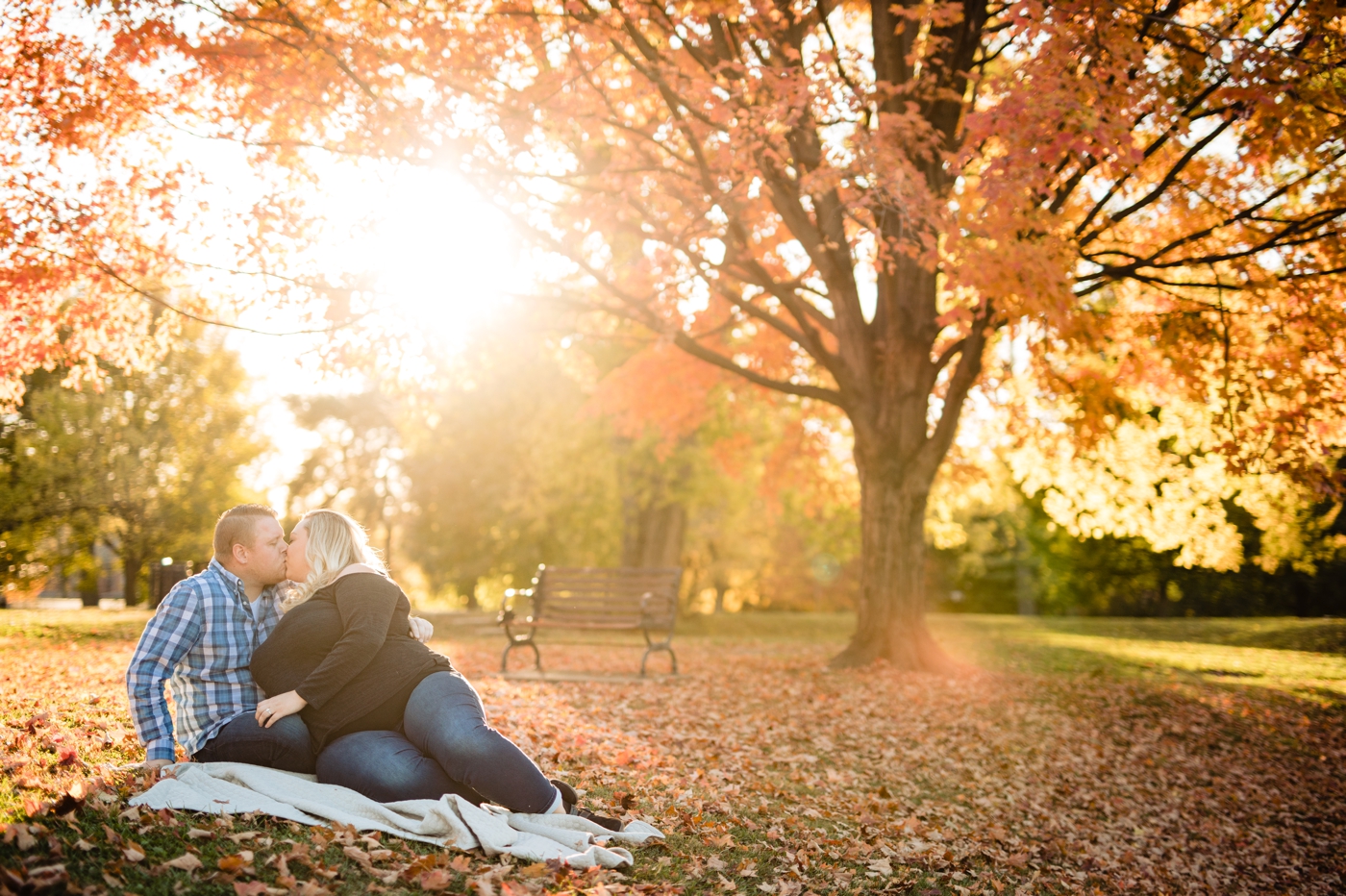a couple kisses beneath an orange fall tree during their Goodale Park engagement photos