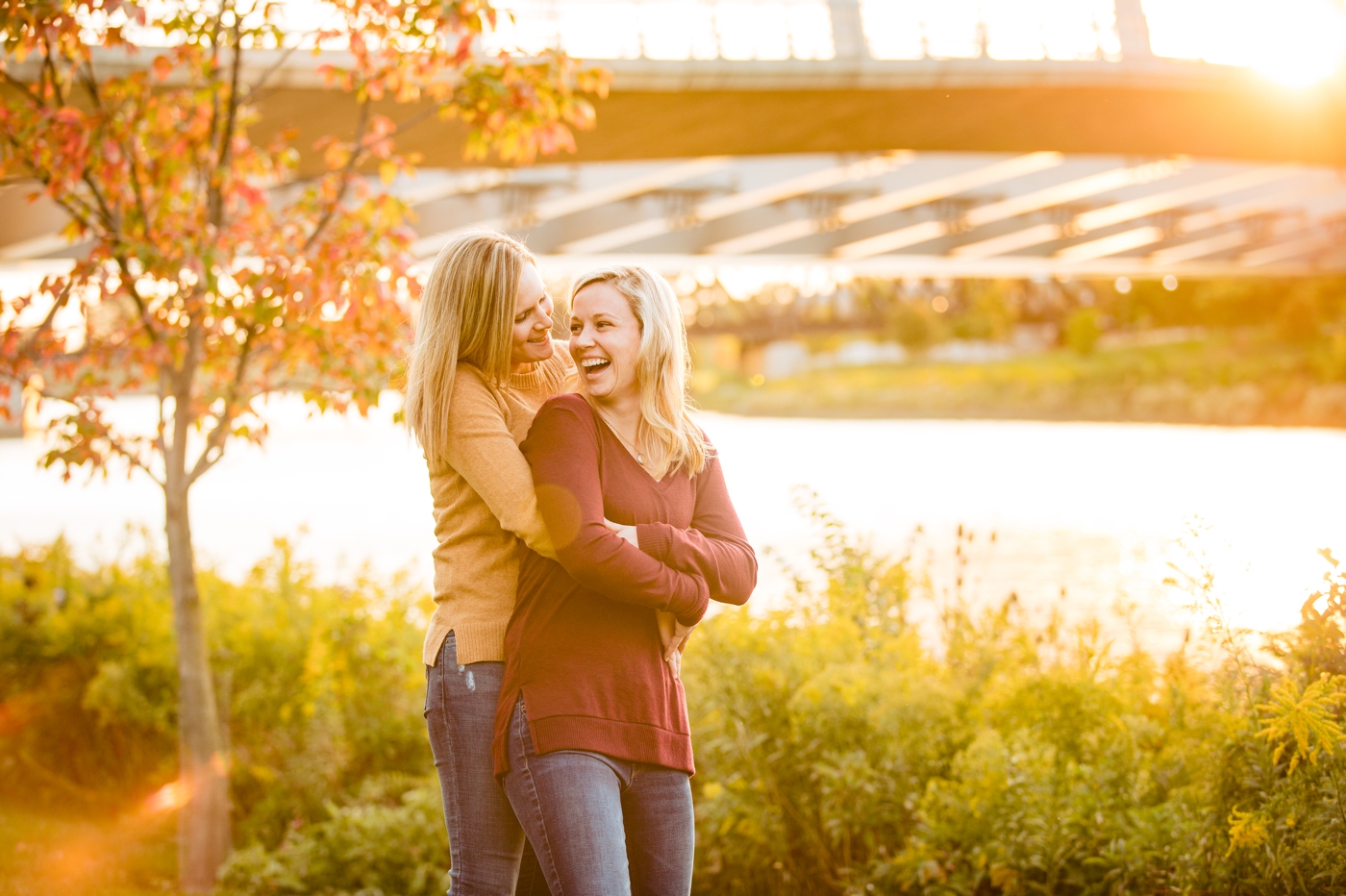 two women pose in front of the bridge and Scioto River during their engagement photos at Bicentennial Park