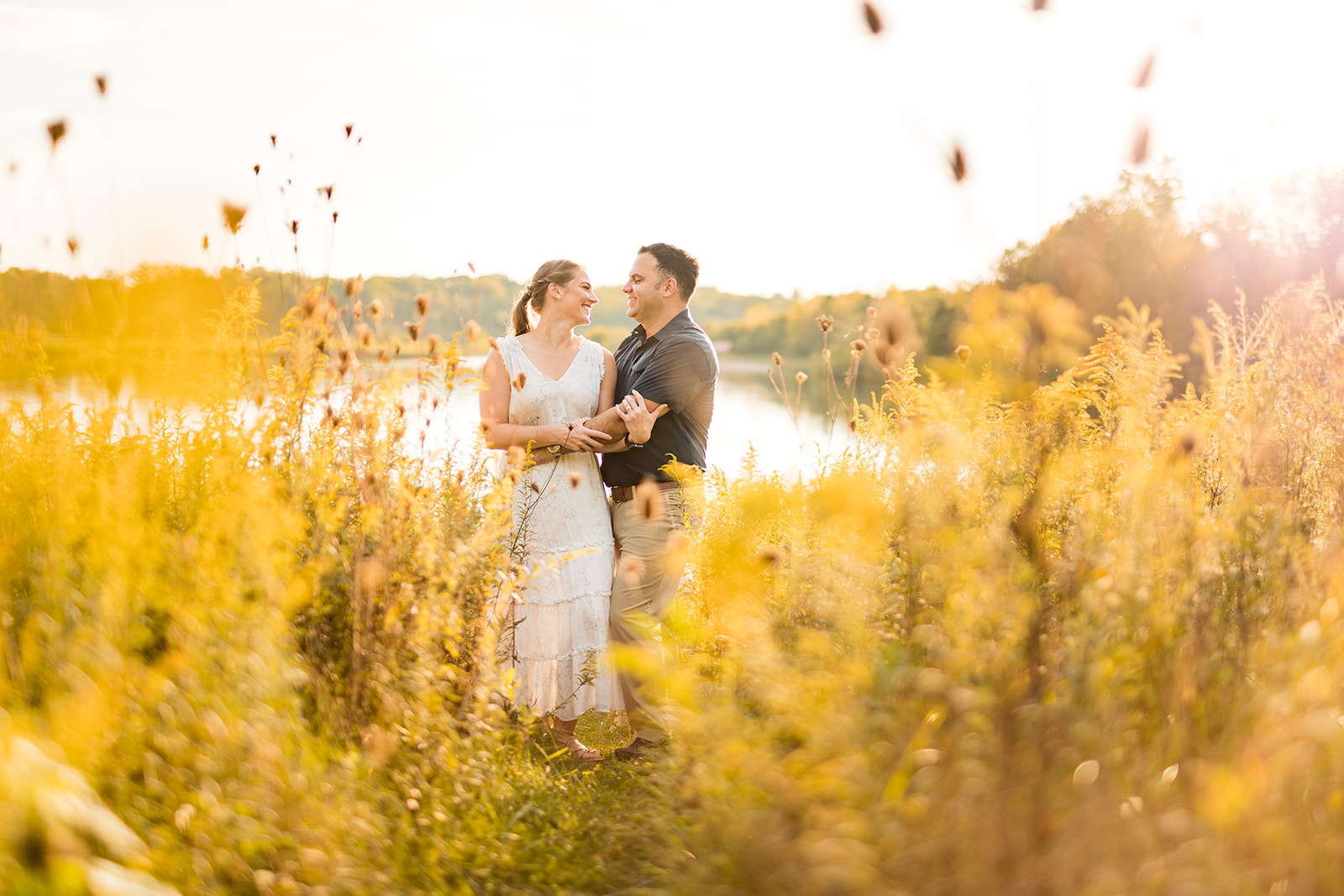 a couple is surrounded by golden rod in front of the setting sun during their engagement photos at Prairie Oaks Metro Park