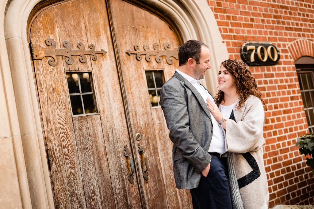 a couple poses in front of large wooden doors during their engagement photos in Worthington