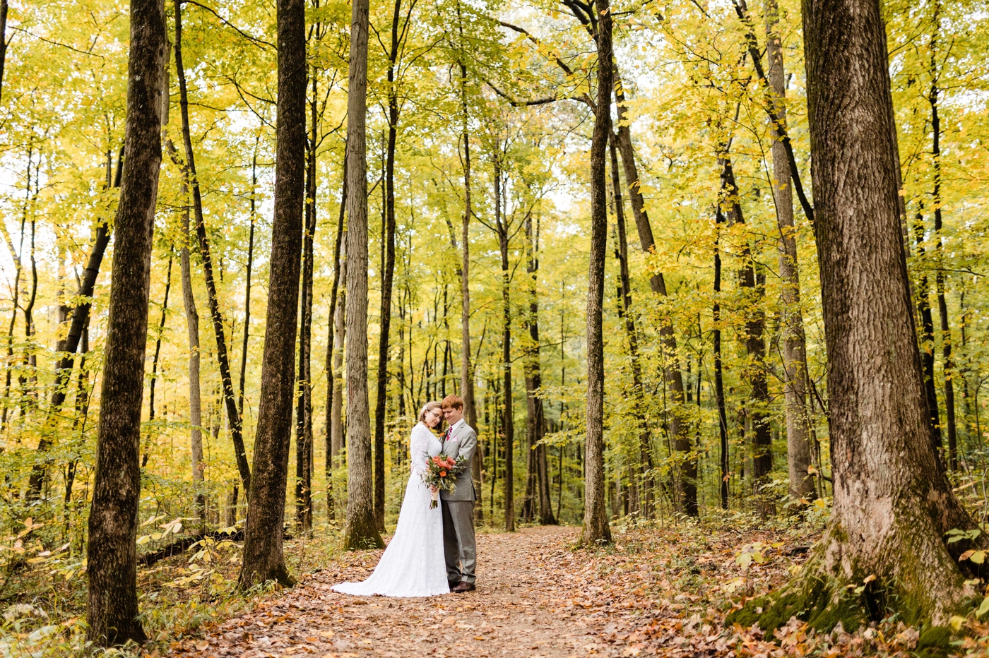 a couple stands among the tall trees before their fall themed wedding at Shadblow Shelter in Blendon Woods