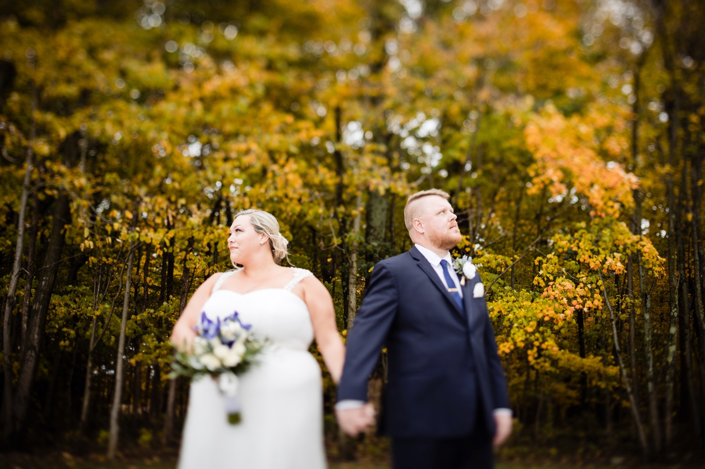 a couple holds hands in front of fall leaves before their wedding at Four Seasons Barn