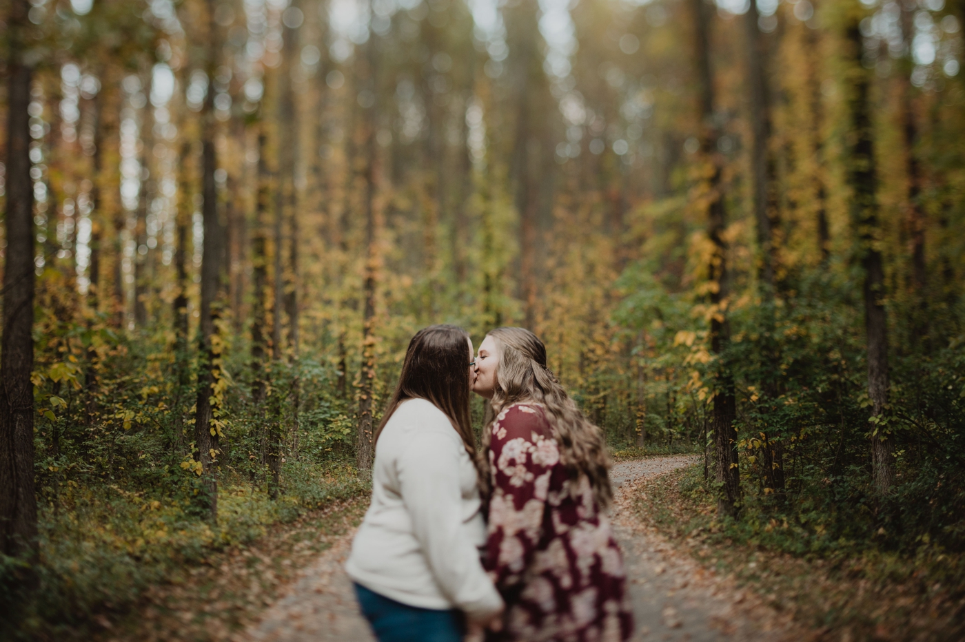 a couple kisses in front of fall foliage during their engagement photos at Walnut Woods