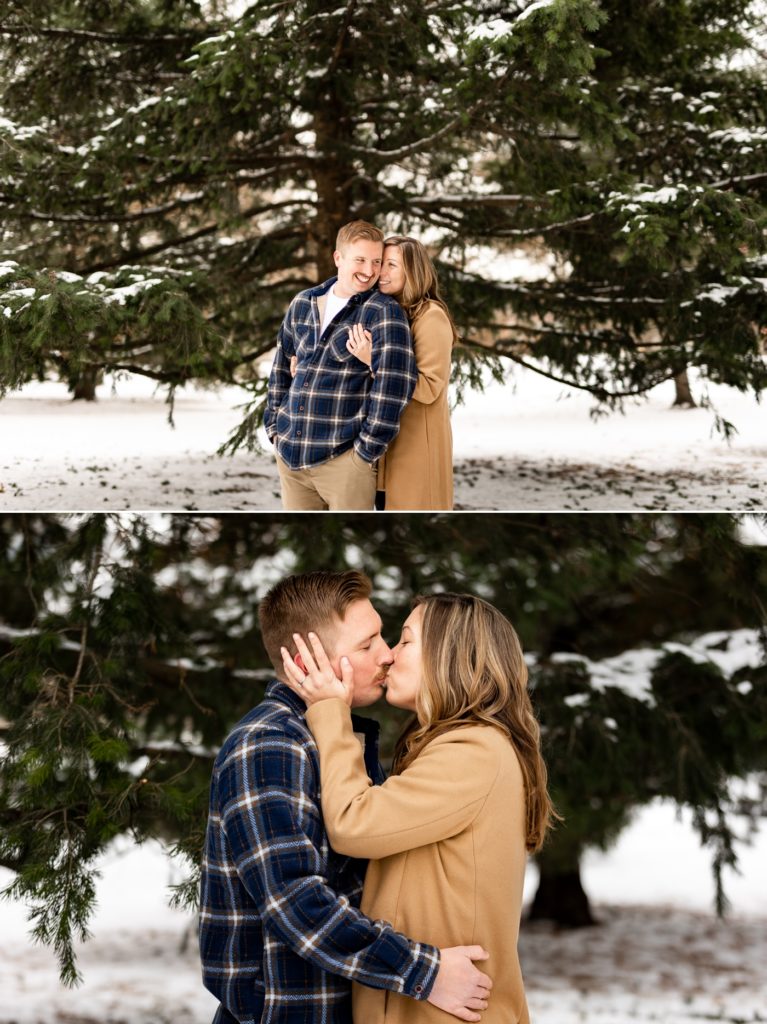a couple kisses in front of pine trees during their snowy Short North engagement photos at Goodale Park