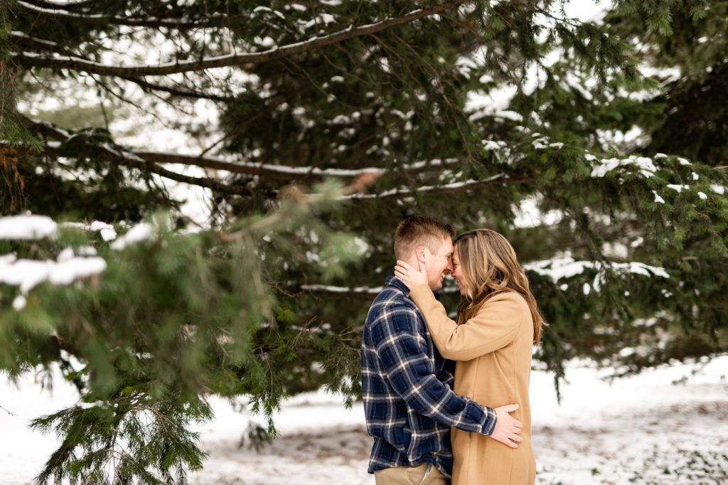 a couple cuddles in the pine trees during their snowy Short North engagement photos at Goodale Park